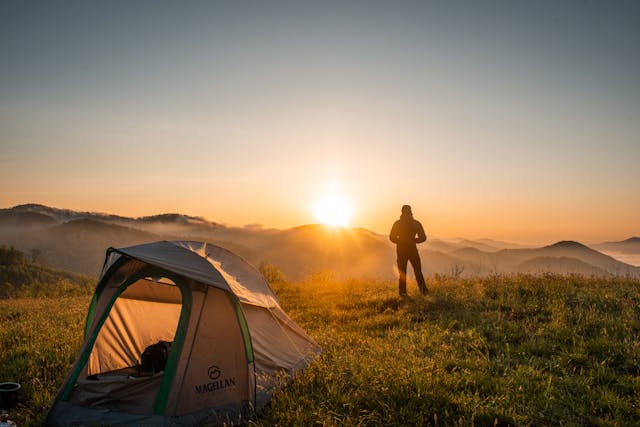 Person standing near a tent at sunrise on a camping trip